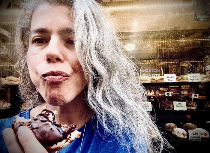 Adicción y Nutrición: Mujer comiendo un pastel cubierto de chocolate frente a una pastelería, representando el deseo por el azúcar y el hambre emocional.