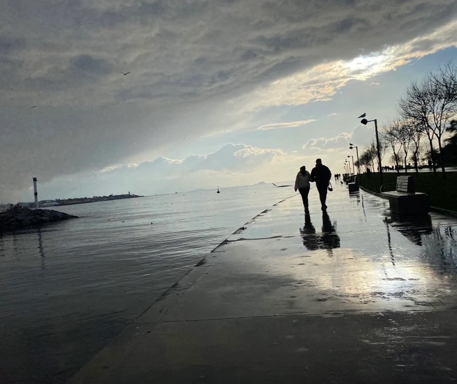 Dos personas caminando junto al mar bajo una luz suave después de la lluvia, reflejando el viaje de la luz interior y la conexión espiritual