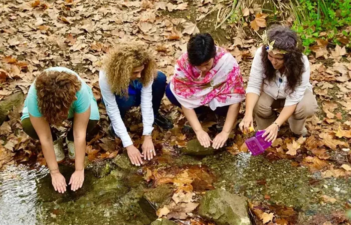 Alumnos de Reiki practicando juntos al aire libre junto a un arroyo entre hojas de otoño.